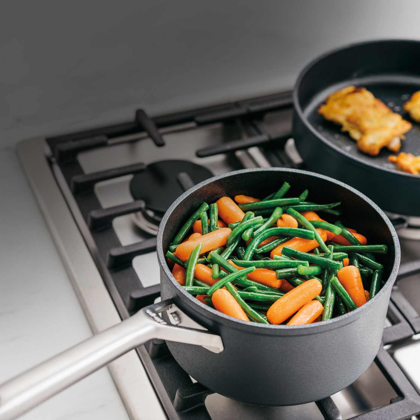 Black Ninja hard anodised saucepan with carrots and green beans cooking on a gas hob